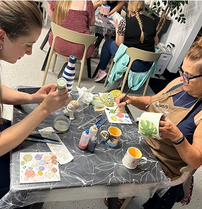 Photo shows two people sitting at a table painting pottery.