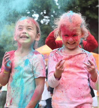 two children at Messy Dash laughing and smiling, covered in paint, slime, water.