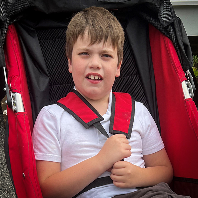 A photo of a young person sitting on the grass at our overnight respite unit for disabled children. The young person is looking at a dinosaur toy.