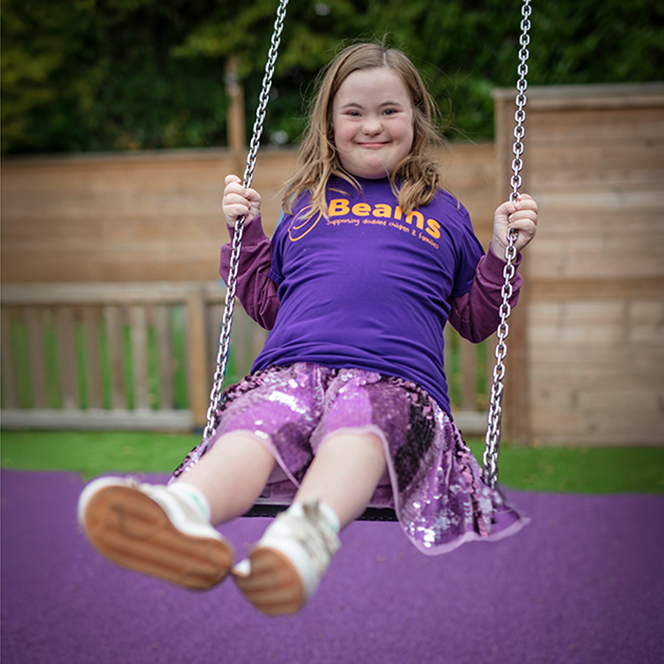 A photo of a young person sitting on the grass at our overnight respite unit for disabled children. The young person is looking at a dinosaur toy.