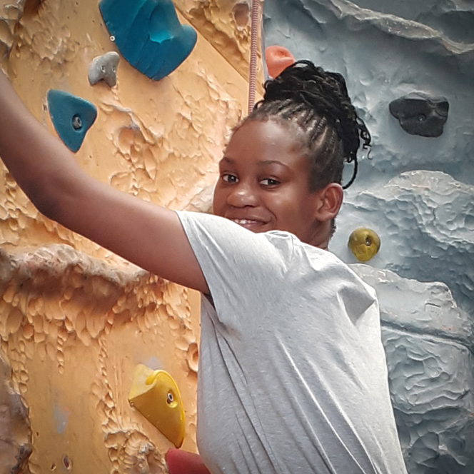 A photo of a young person sitting on the grass at our overnight respite unit for disabled children. The young person is looking at a dinosaur toy.
